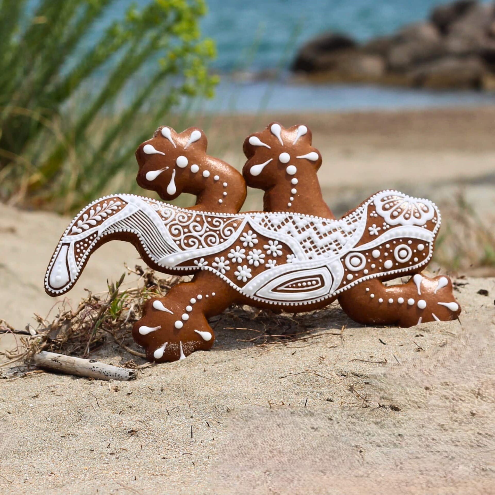 Biscuit décoré en forme de lézard artistiquement glacé, posé sur le sable devant un paysage côtier paisible