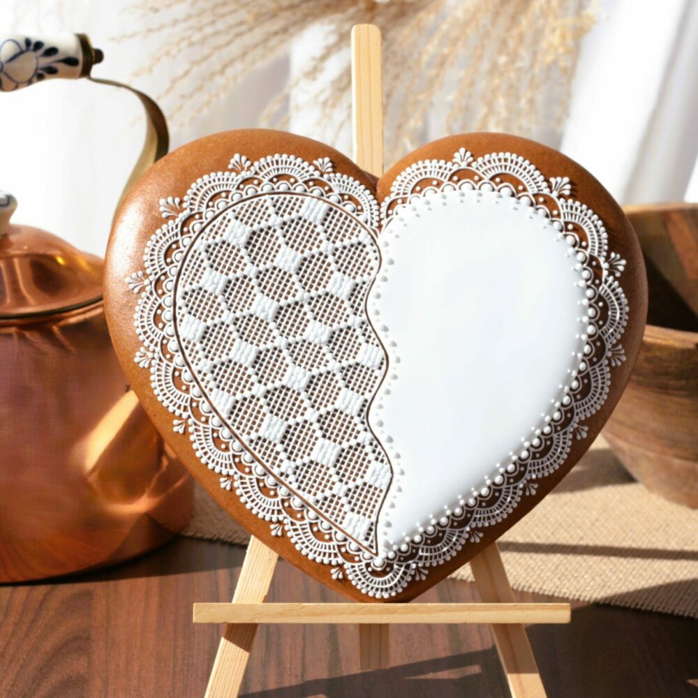 Biscuit décoré en forme de cœur avec glaçage blanc détaillé, exposé sur un chevalet, accompagné d'une théière en cuivre et d'ustensiles en bois