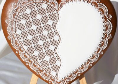 Biscuit décoré en forme de cœur avec des motifs détaillés en glaçage blanc, posé sur un chevalet.