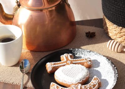 Biscuit décoré en forme de croix camarguaise sur une assiette noire, accompagné d'une tasse de café et d'une théière en cuivre, créant une ambiance conviviale et raffinée.