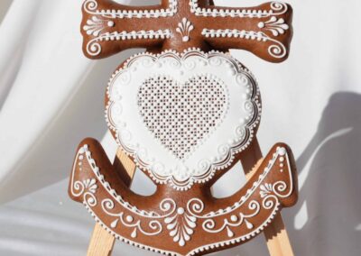 Biscuit décoré en forme de croix d'Occitanie avec un cœur au centre, orné de motifs en glaçage blanc, posé sur un chevalet, capturant l'élégance et la tradition pâtissière.