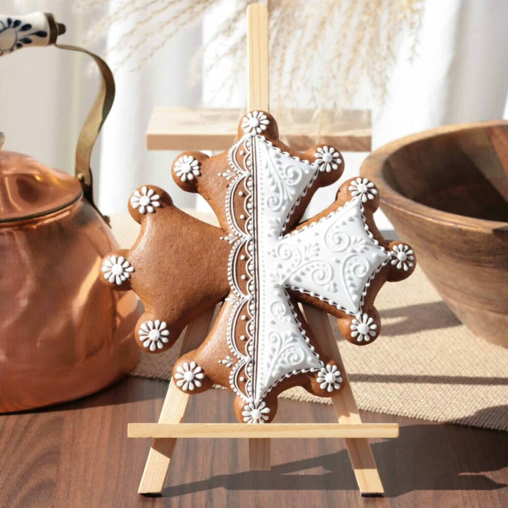 Biscuit en forme de croix d'Occitanie, décoré avec des motifs en glaçage blanc, posé sur un chevalet, avec une théière en cuivre et un bol en bois en arrière-plan.