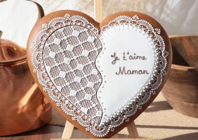 Biscuit en forme de cœur décoré, personnalisé avec l'inscription "Je t'aime Maman", exposé sur un chevalet.