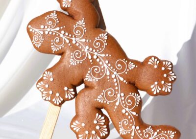 Biscuit en forme de lézard avec des motifs délicats en glaçage blanc, posé sur un chevalet, capturant l'art raffiné de la pâtisserie décorative.