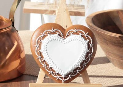 Biscuit en forme de cœur, finement décoré de motifs en glaçage blanc, posé sur un chevalet avec une théière en cuivre en arrière-plan