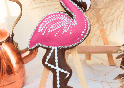 Biscuit en pain d'épices en forme de flamant rose, décoré avec un glaçage rose et blanc aux motifs détaillés, présenté sur un chevalet en bois.